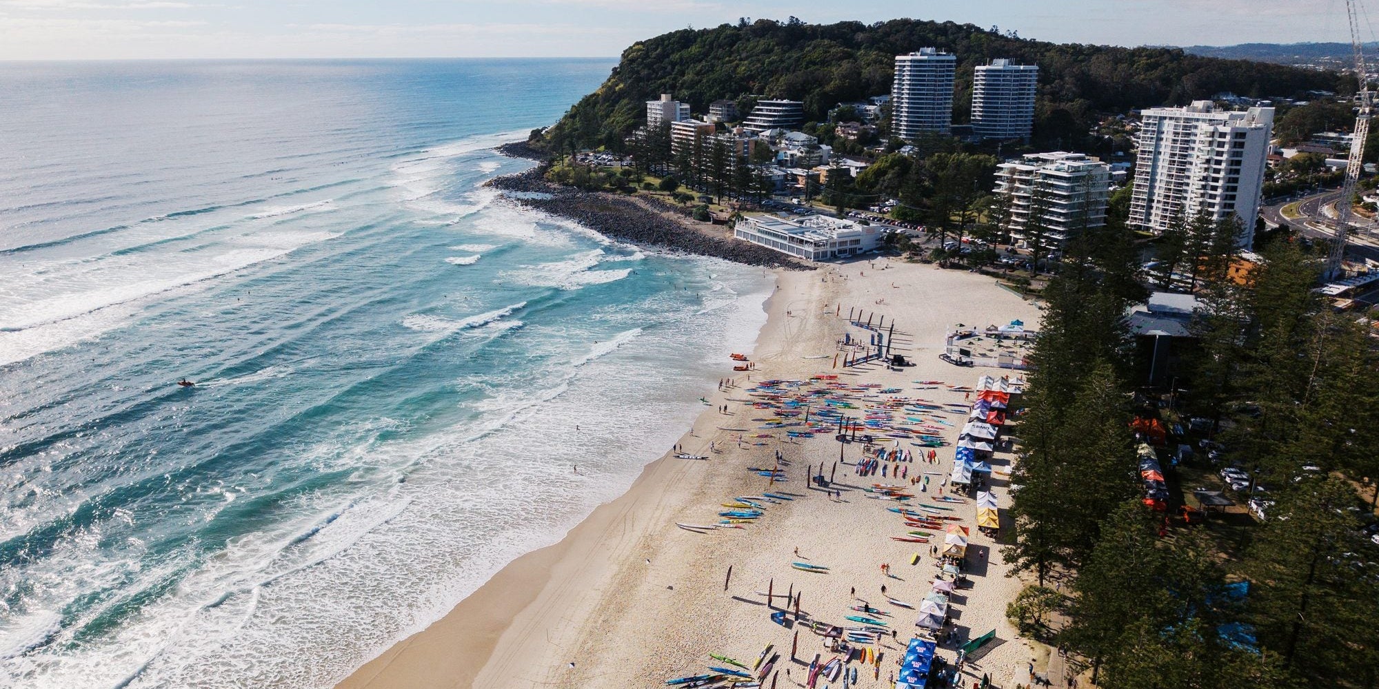 Drone view of Burleigh Beach with craft lined up on the sand and Burleigh headland behind