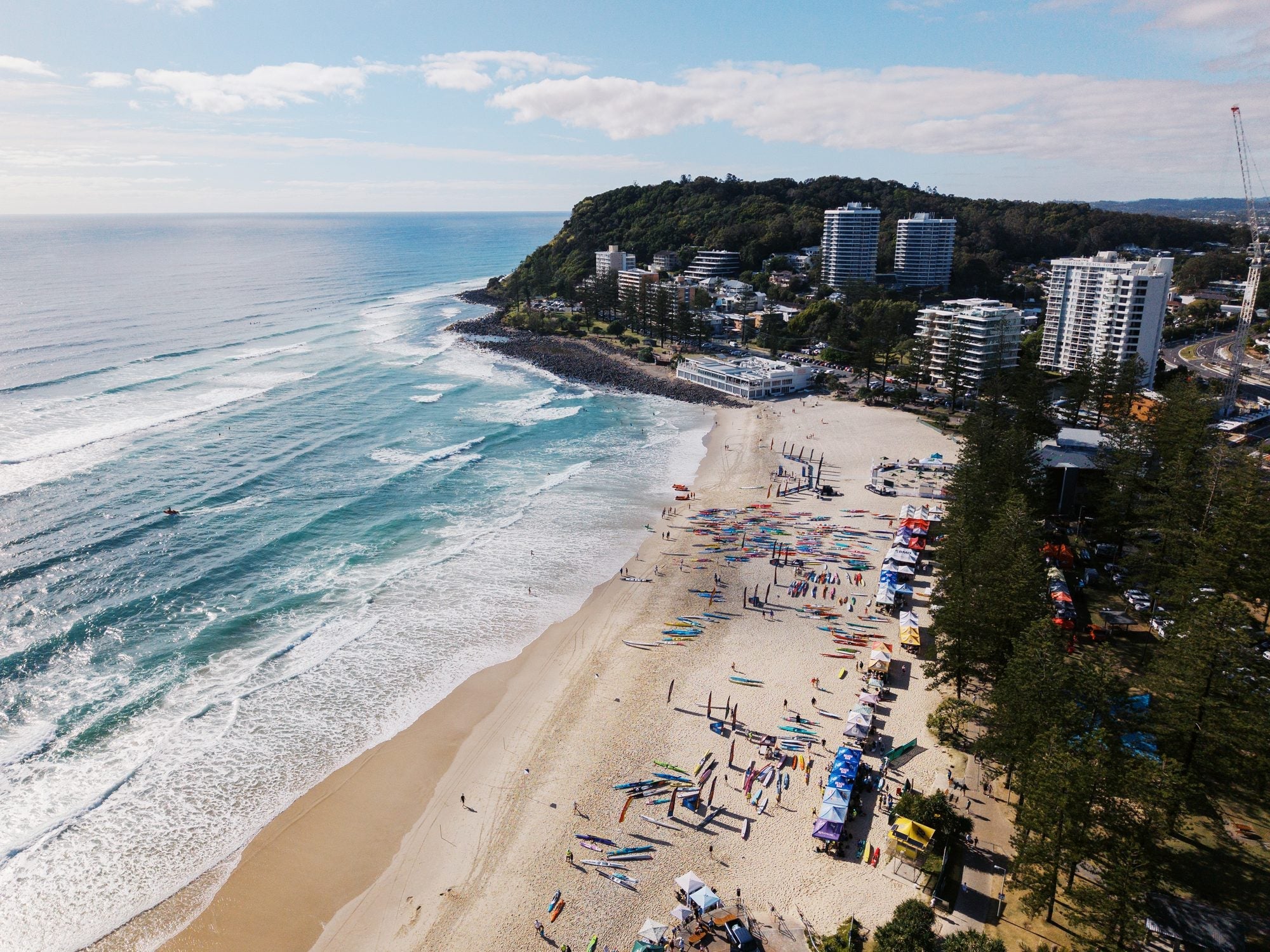 Drone view of Burleigh Beach with craft lined up on the sand and Burleigh headland behind