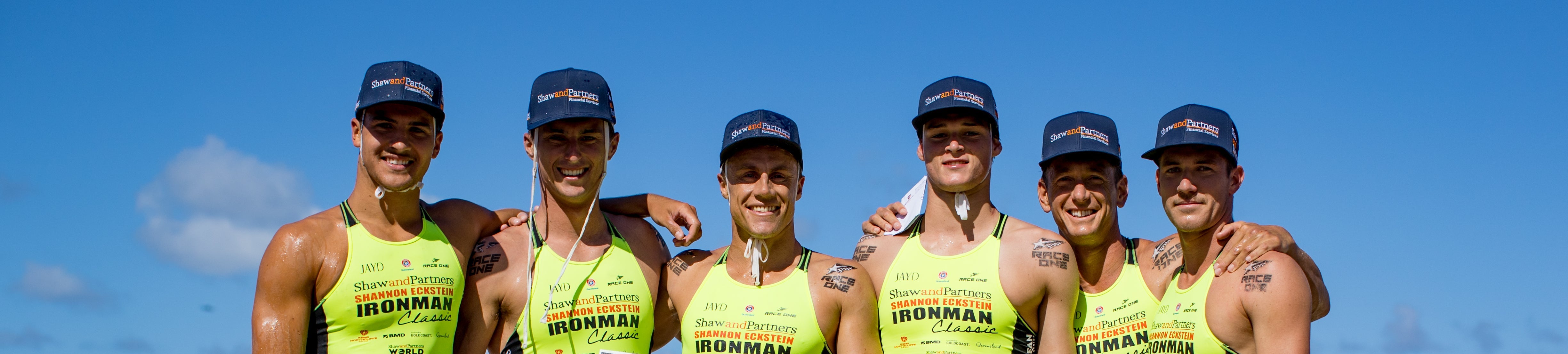 Shaw and Partners Athletes holding large cheques on a beach with a clear sky